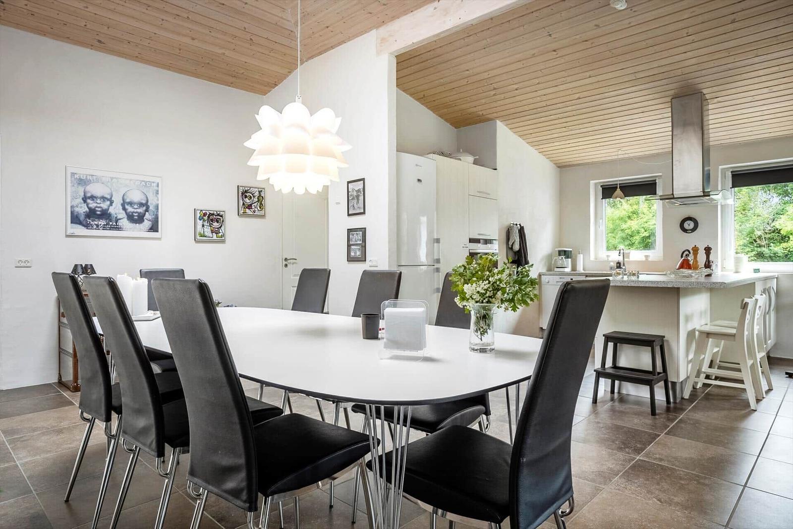 Dining room with white table and black chairs, kitchen island, and wooden ceiling.