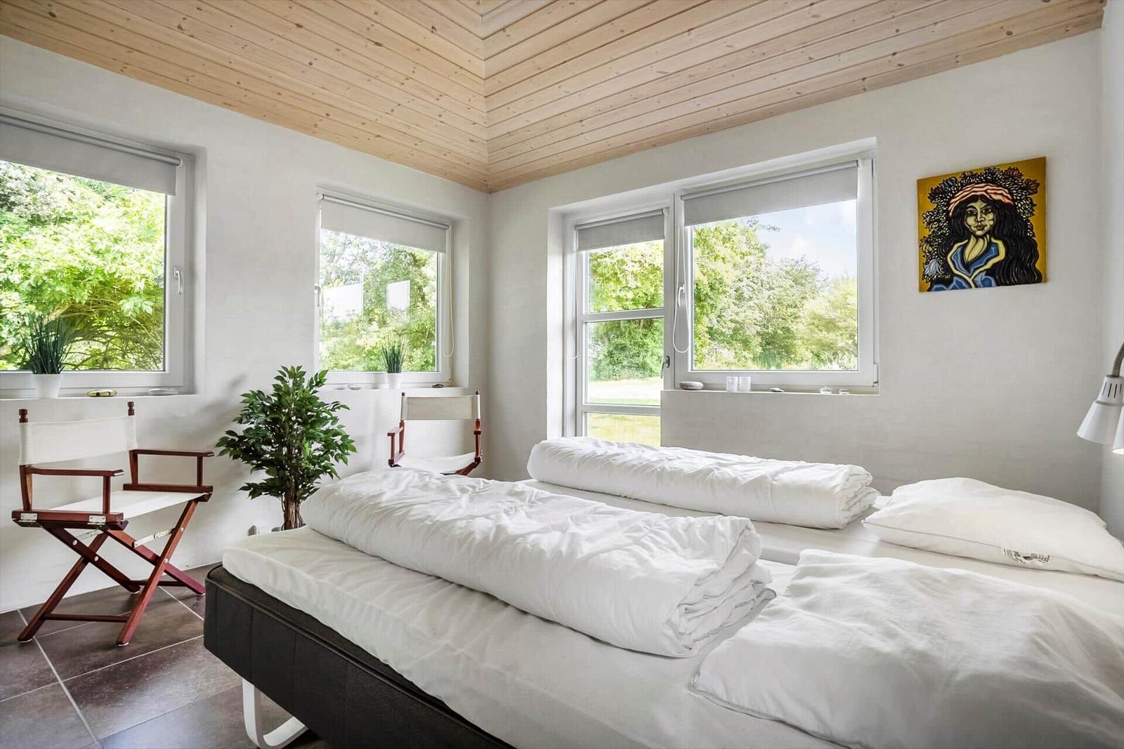 Room with two beds, wooden ceiling, and windows to greenery.