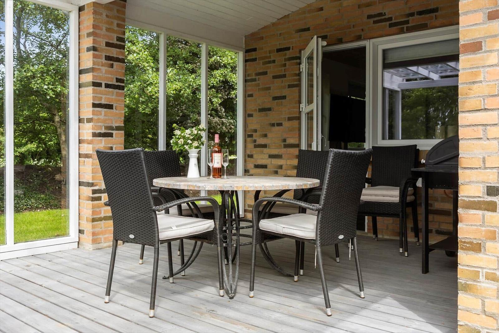Patio with table, chairs, and grill. View of green surroundings.