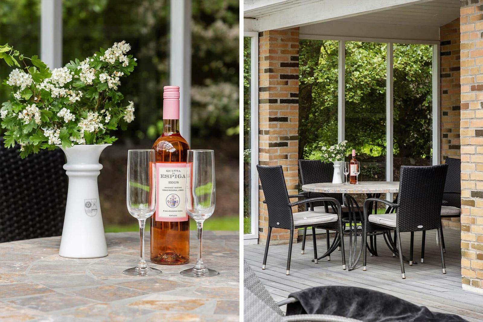 Outdoor area with table, chairs, and flowers. Bottle of wine and two glasses.