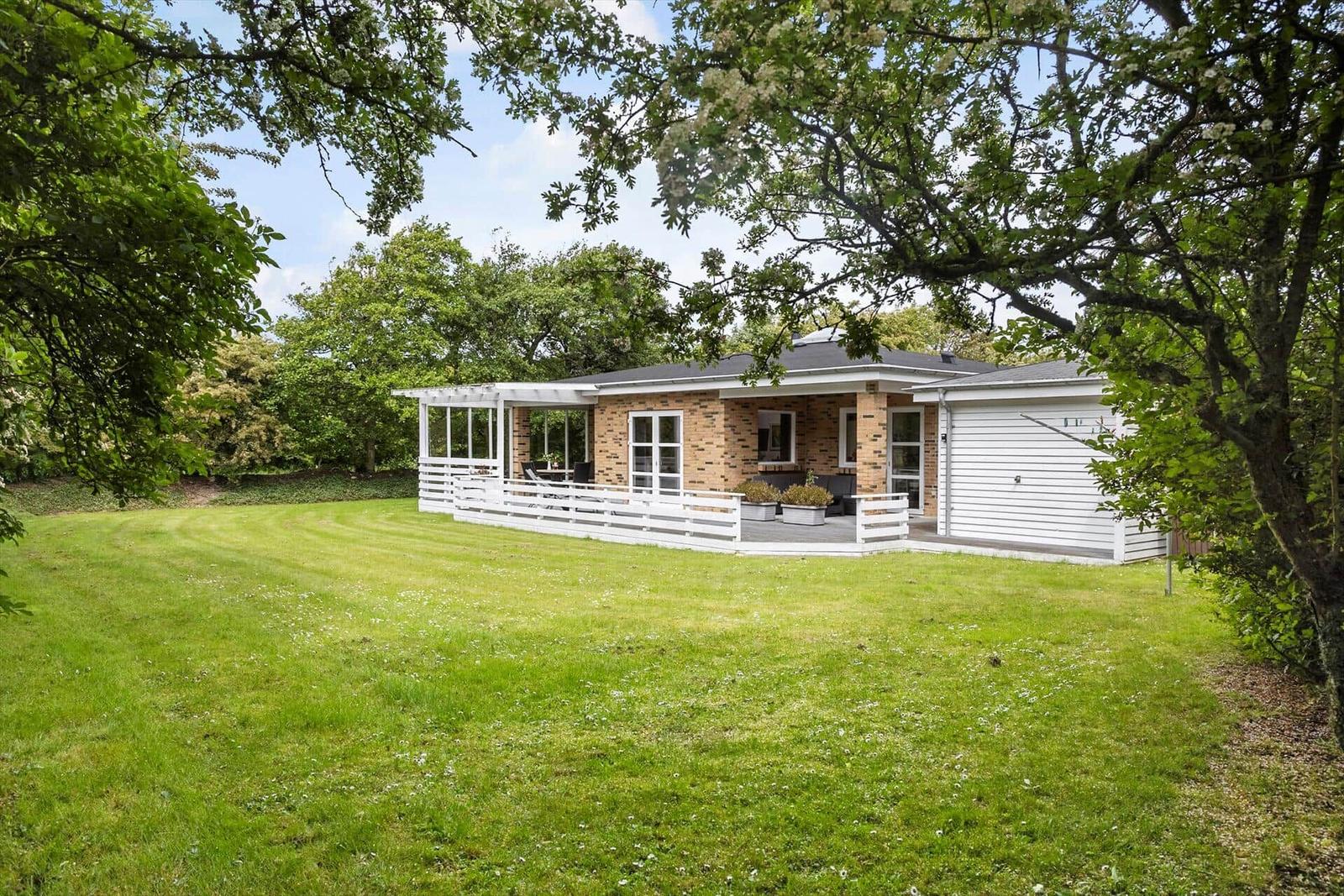 A house with terrace and garage on a green lawn surrounded by trees.
