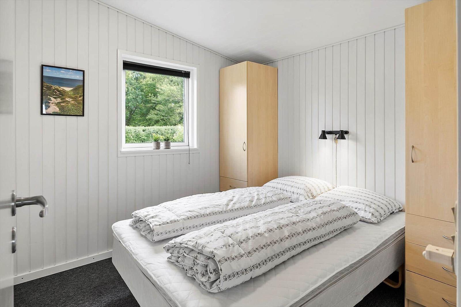 Bedroom with double bed, window, and wooden wardrobe.