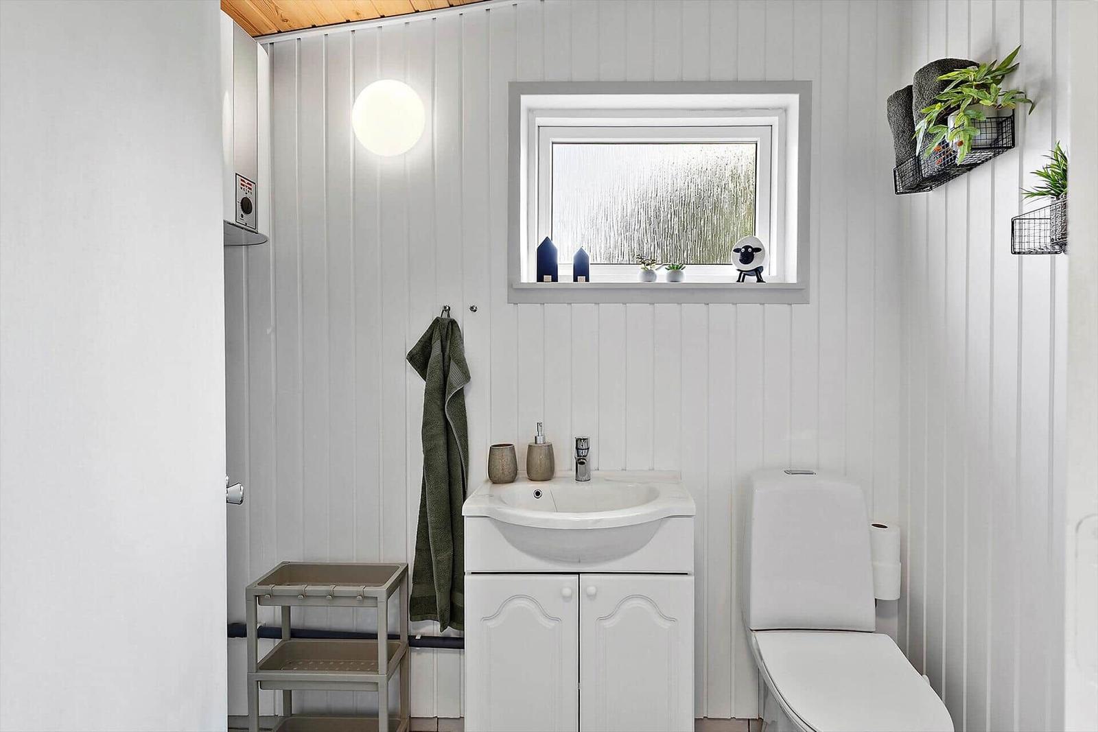 Bathroom with sink, toilet, and shower. Window with plants and decor.