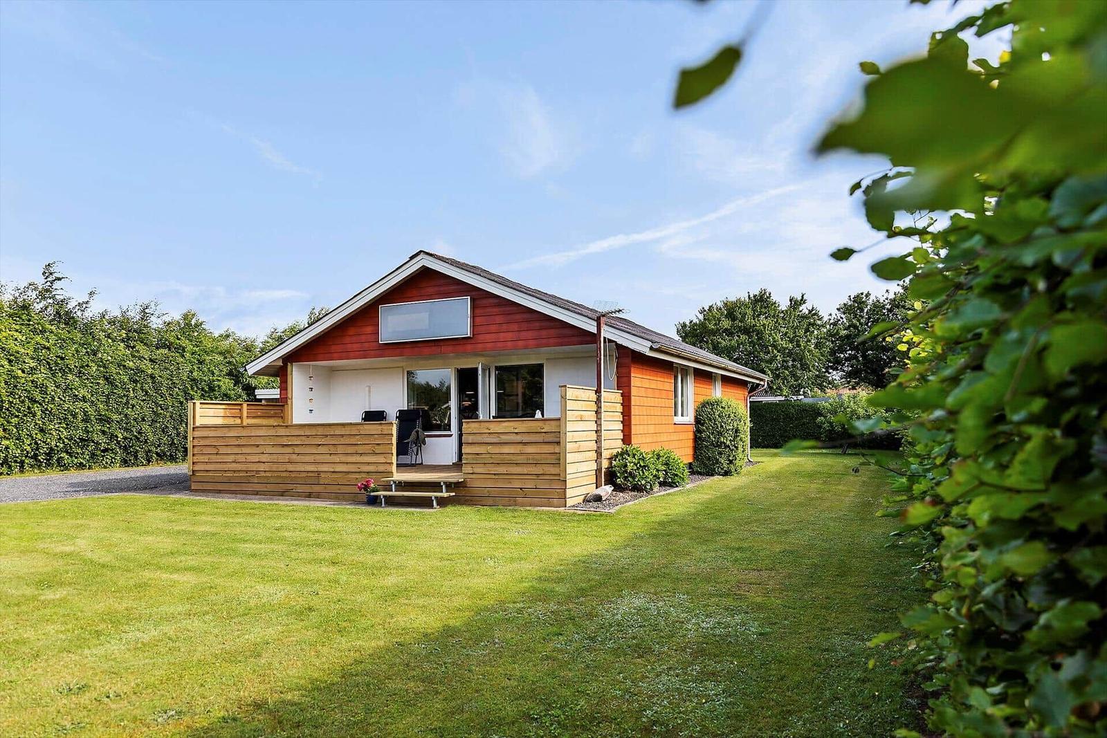 A house with a red roof and wooden terrace on green grass.