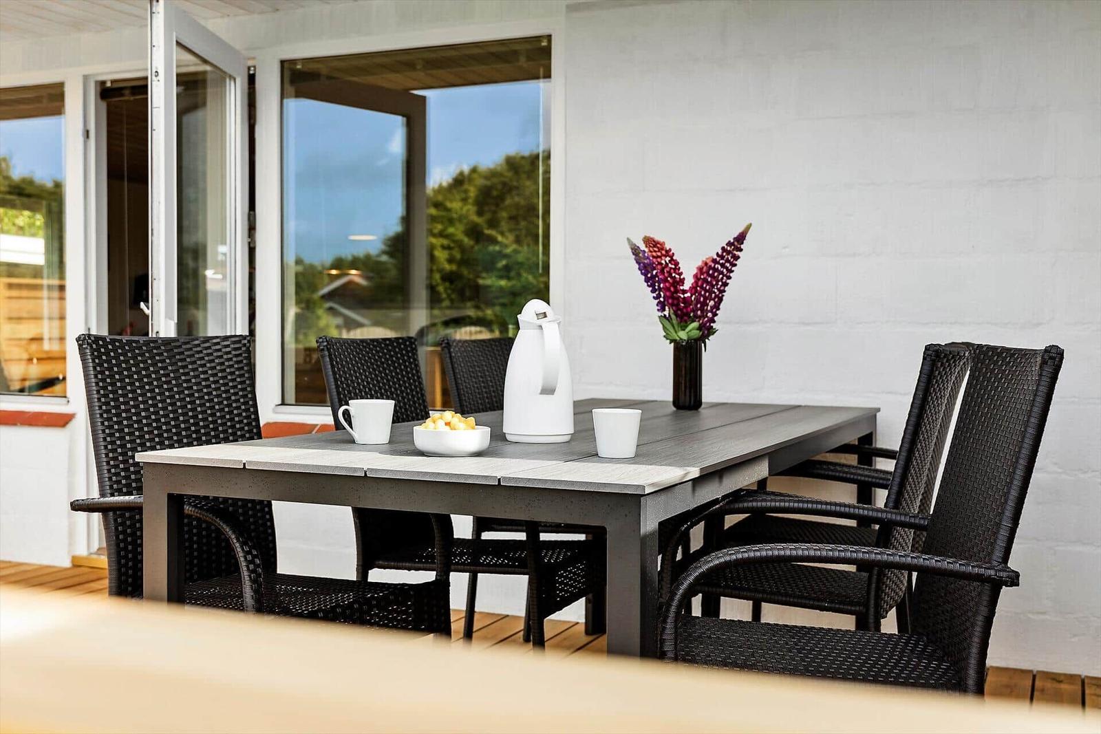 Terrace with table and chairs, vase with flowers and thermos.