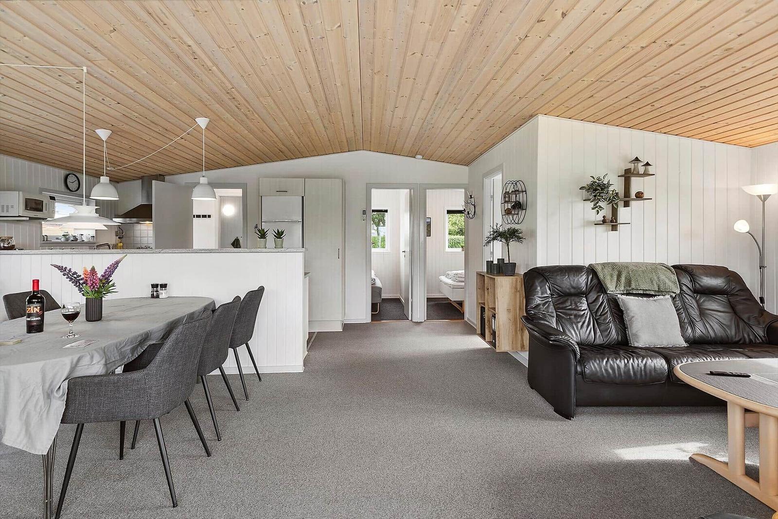 Living and dining area with kitchen and sofa under wooden ceiling.
