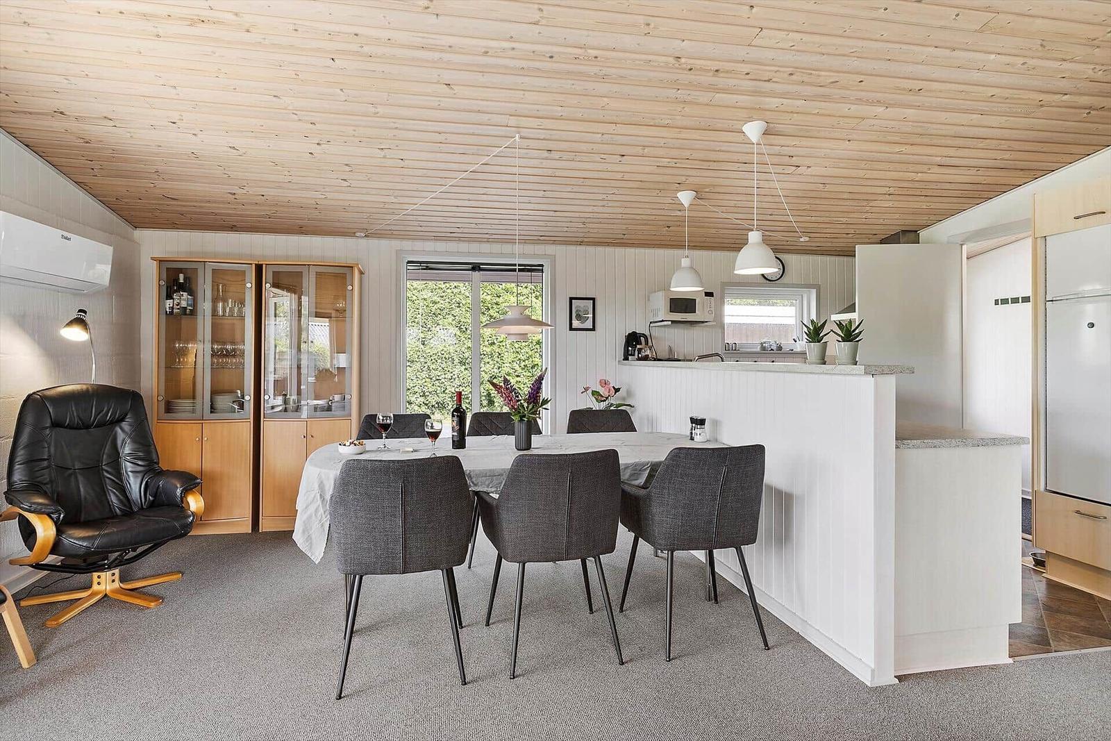 Dining area with table, chairs, and kitchen island. Wooden ceiling and window with view outside.