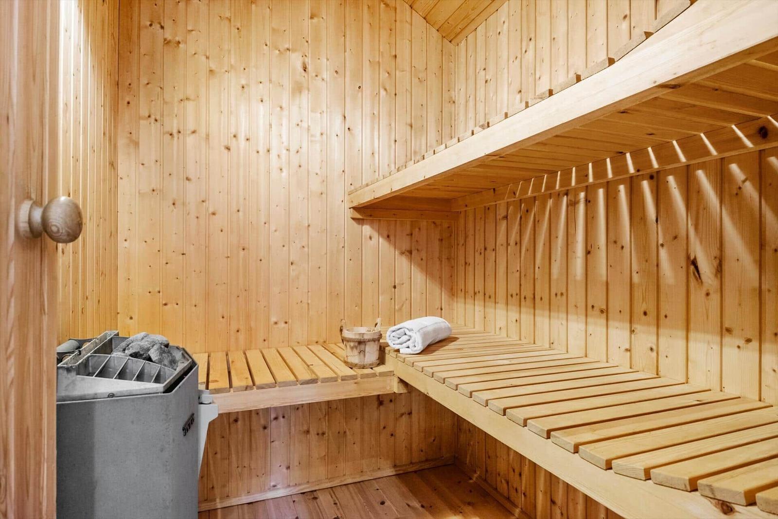 Sauna mit Holzbank und Holzwand, daneben Heizung und Eimer mit Handtuch.