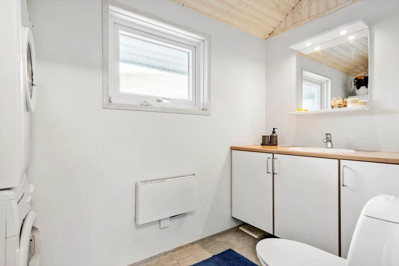 Badezimmer mit Waschmaschine, Waschtisch und Toilette. Holzdecke und Fenster.