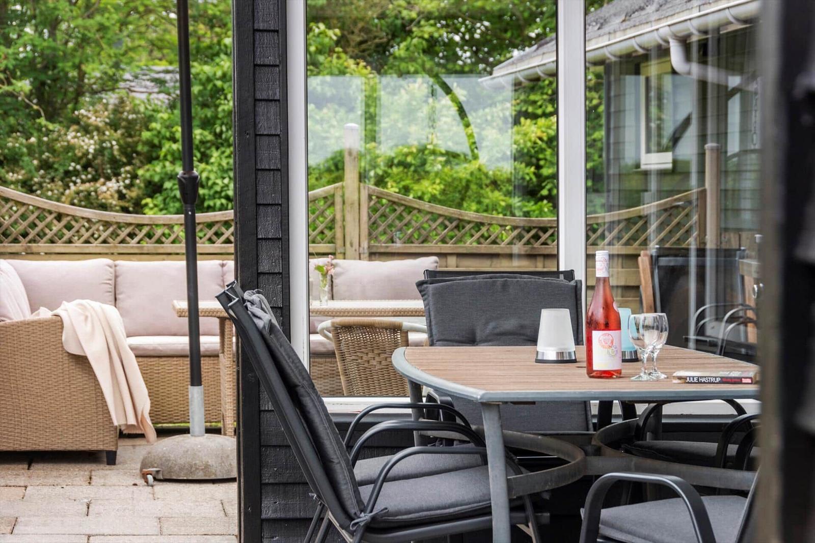 Terrasse mit Tisch, Stühlen und Sitzbank. Hintergrund mit Grün und Holzgeländer.