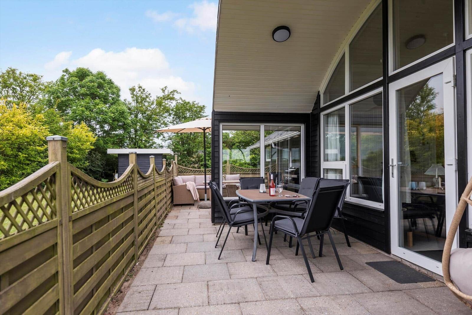 Terrasse mit Tisch, Stühlen und Sitzgelegenheit. Holzgeländer und Garten im Hintergrund.