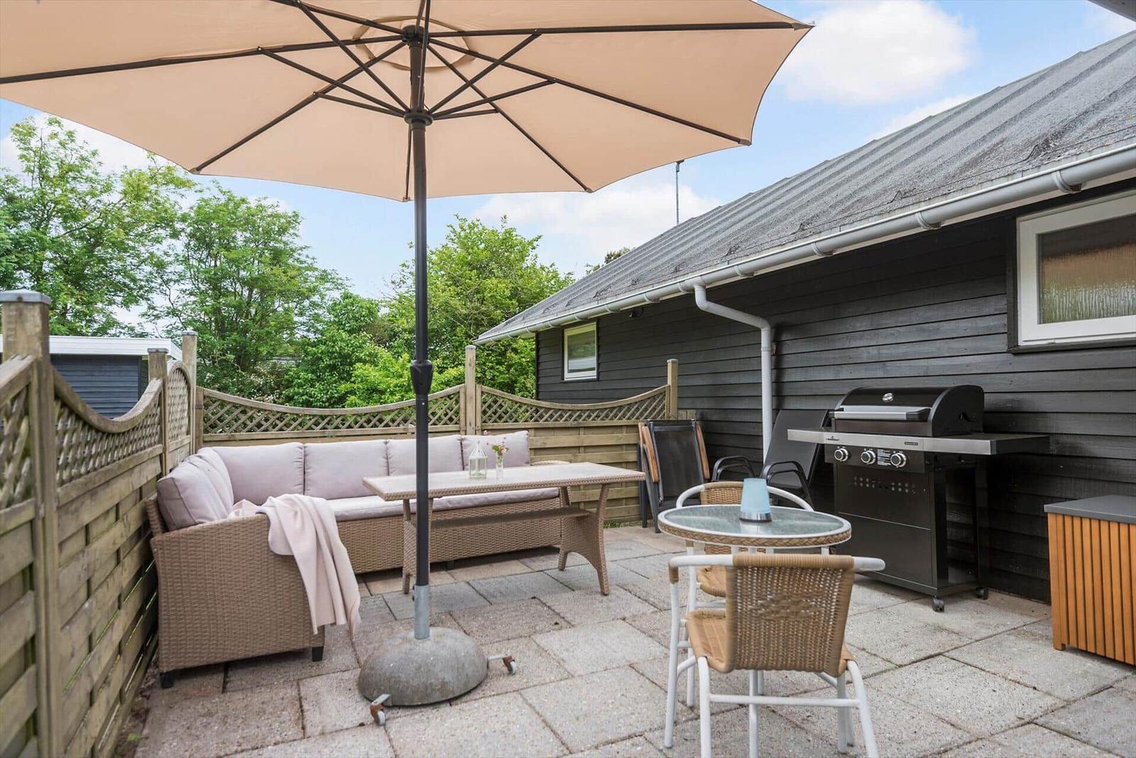 Terrasse mit Sitzgruppe, Sonnenschirm, Grill und Holzgeländer.