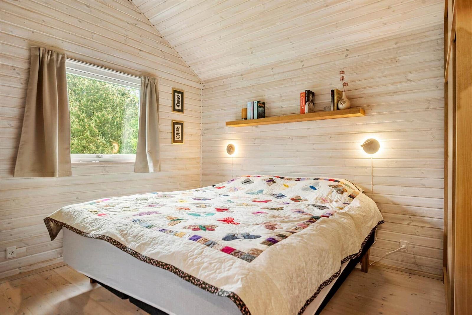 Schlafzimmer mit Holzwand, Bett und Fenster. Regal mit Büchern und Lampe.