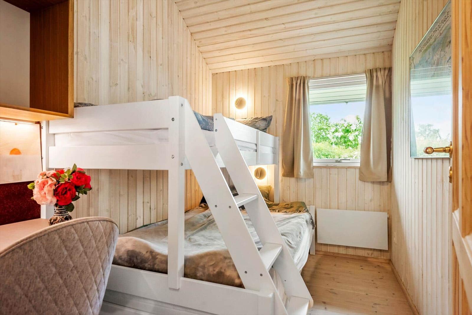 Zimmer mit Doppelstockbett, Holzwand und Fenster mit Blick auf Grün.