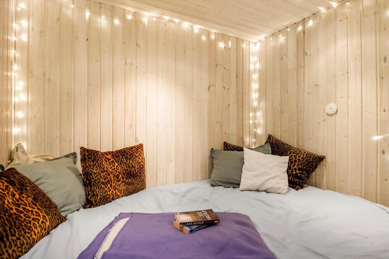 Schlafzimmer mit Holzwand, Bett, Kissen und Lichterkette.