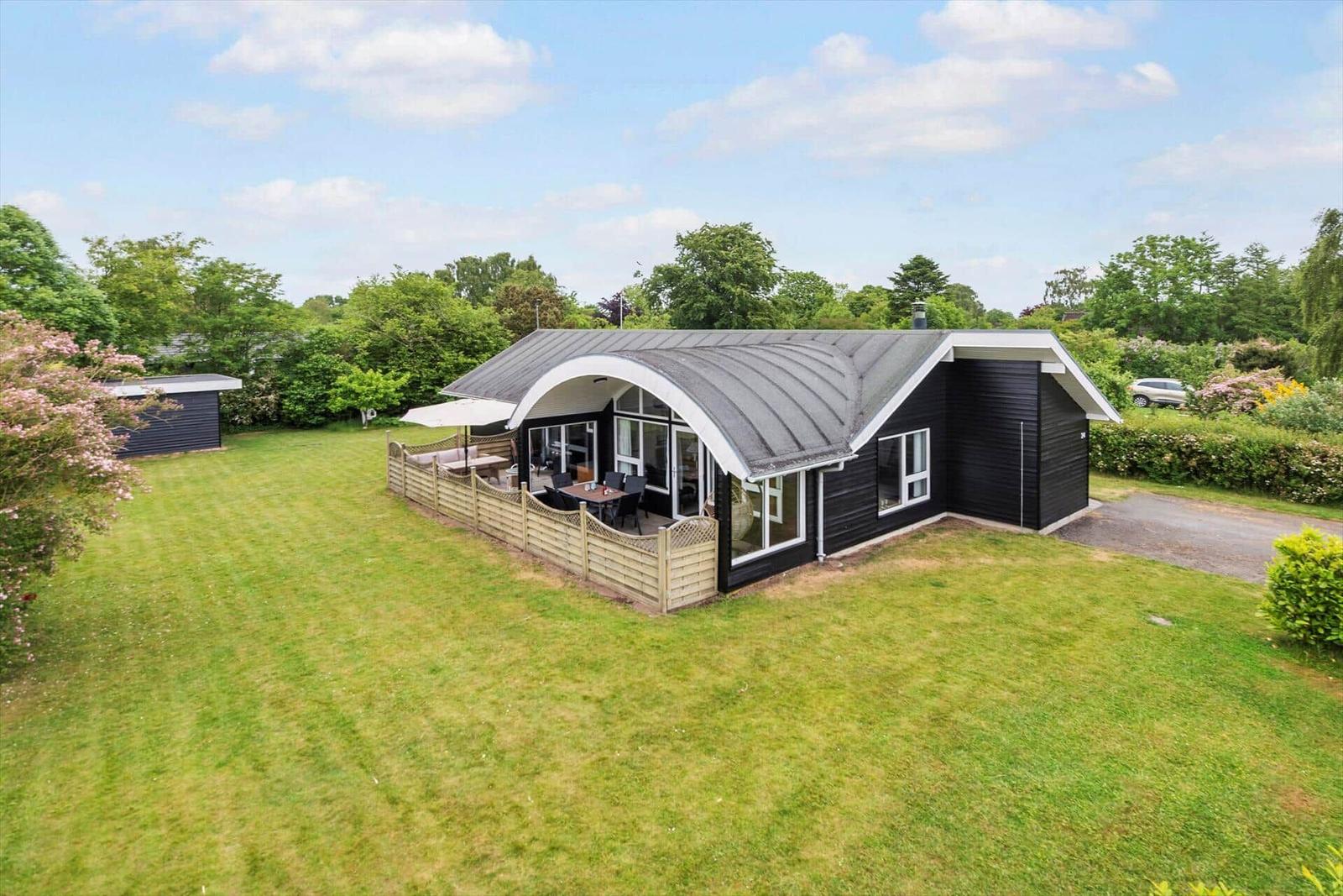 Moderne schwarze Hütte mit großem Garten und Terrasse unter Bogenüberdachung.