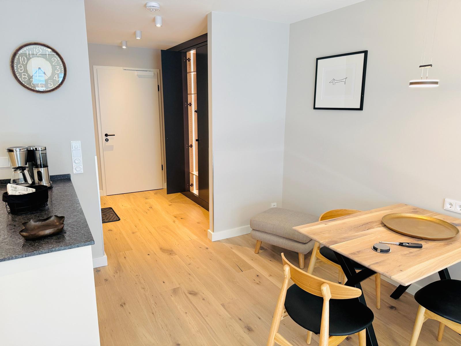 Essbereich mit Holztisch, Stühlen und Wandbild. Küchenzeile mit Kaffeemaschine. Holzfußboden und Schrank.