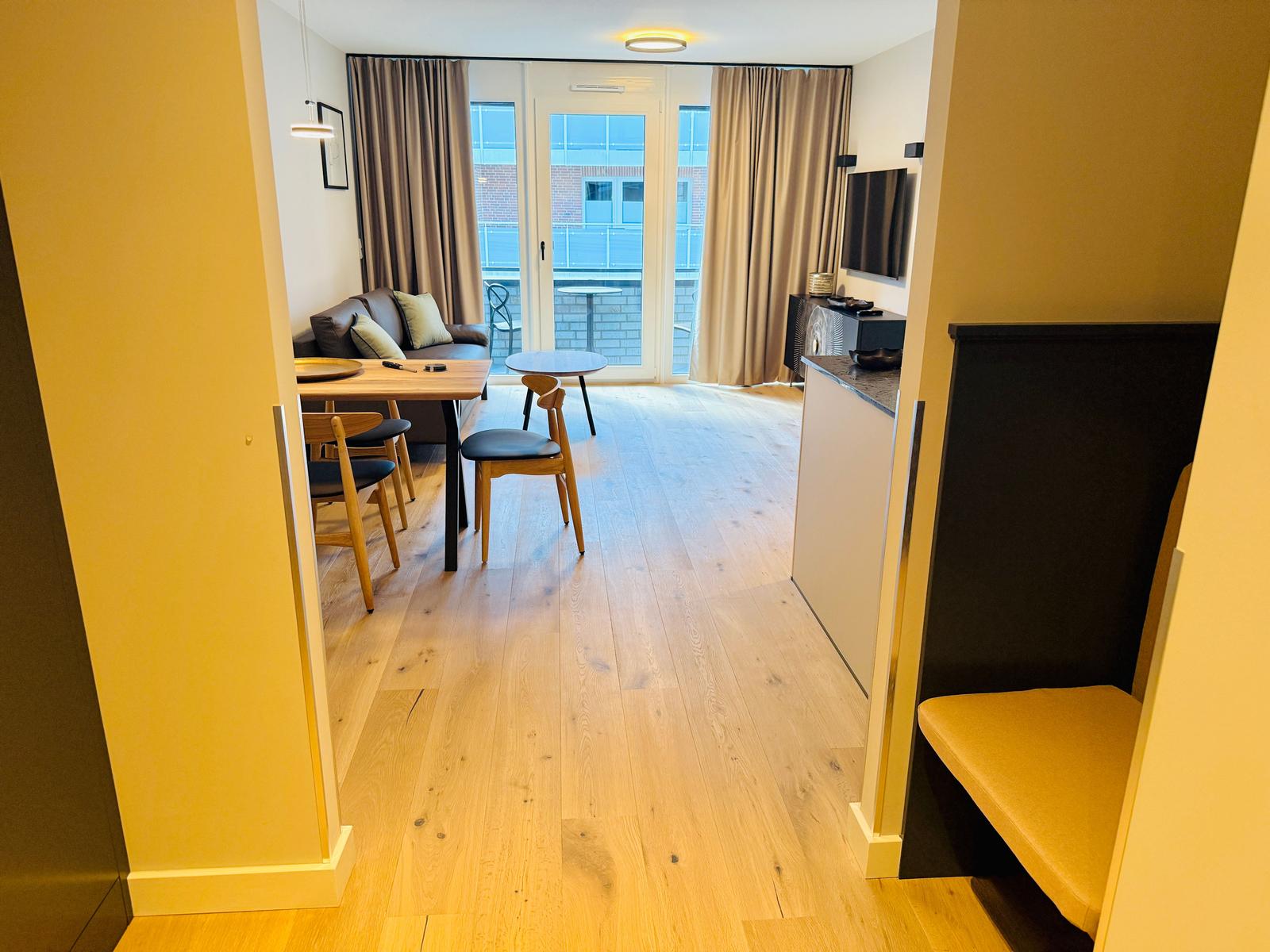 Wohnbereich mit Esstisch, Sofa und Balkon. Holzfußboden und TV.