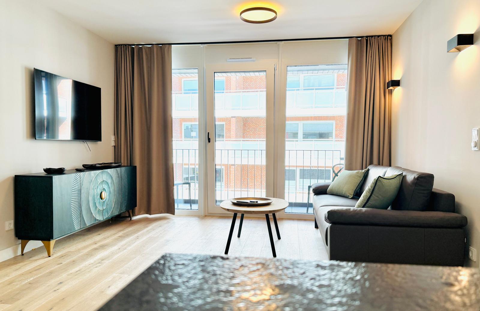 Wohnzimmer mit Sofa, Fernseher und Balkonansicht