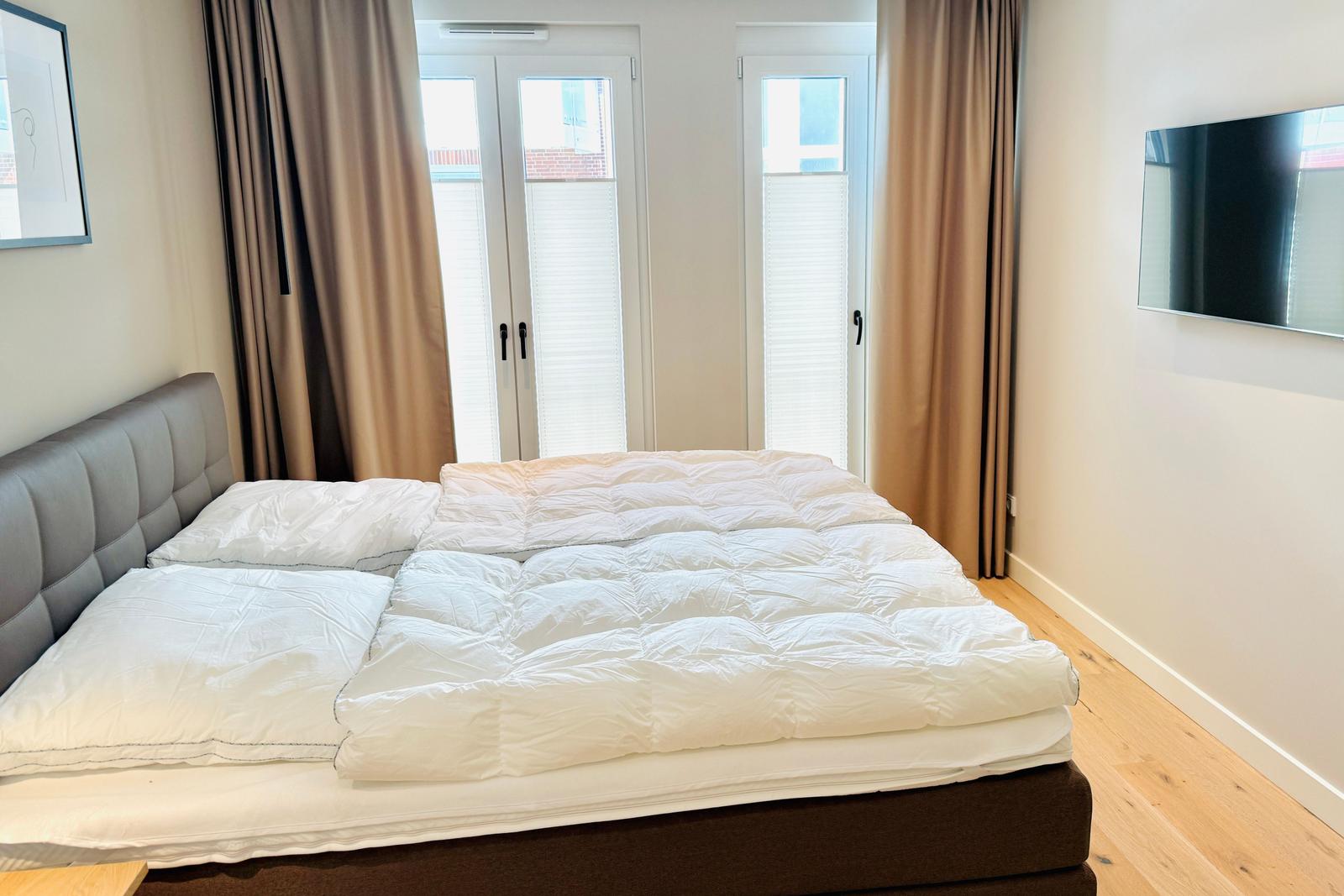 Schlafzimmer mit Bett, TV und Fenster mit Vorhängen.