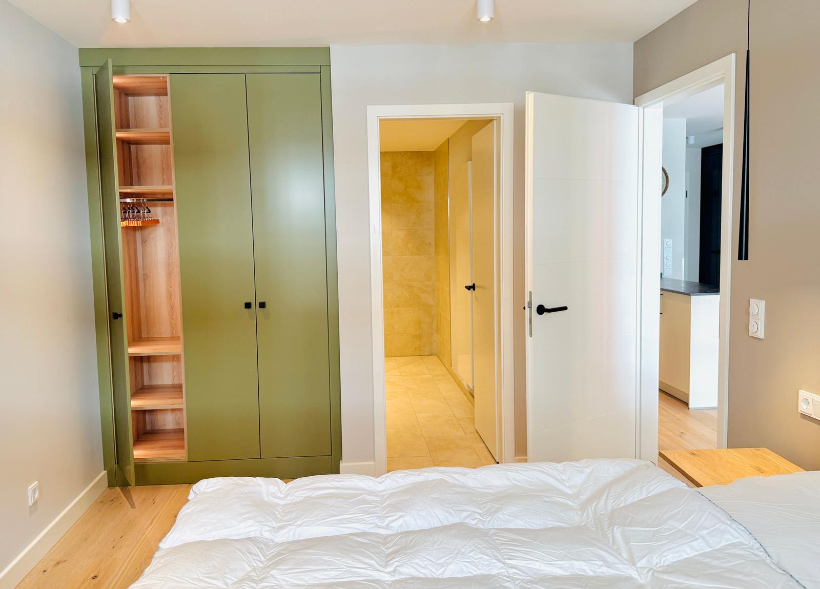 Schlafzimmer mit grünem Schrank, Blick in Bad und Küche