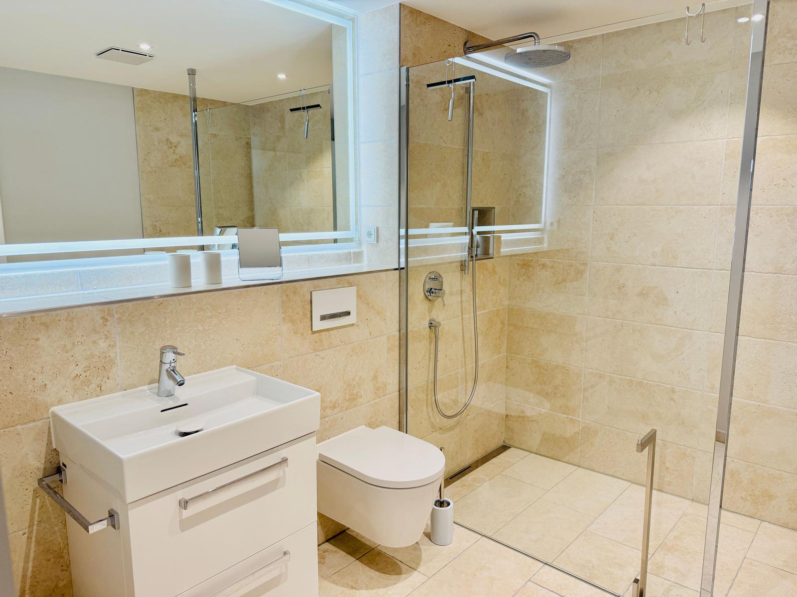 Bad mit Dusche, Waschbecken und Toilette. Fliesenwand und Spiegel.