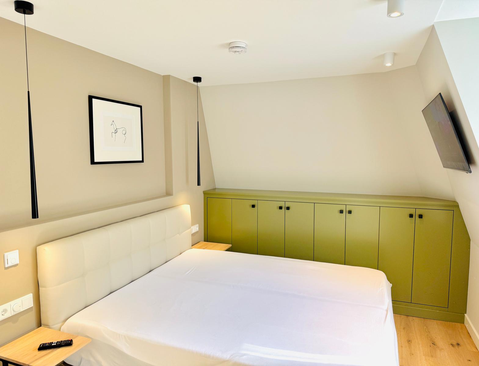 Schlafzimmer mit Bett, grüner Schrank und Wandbild.