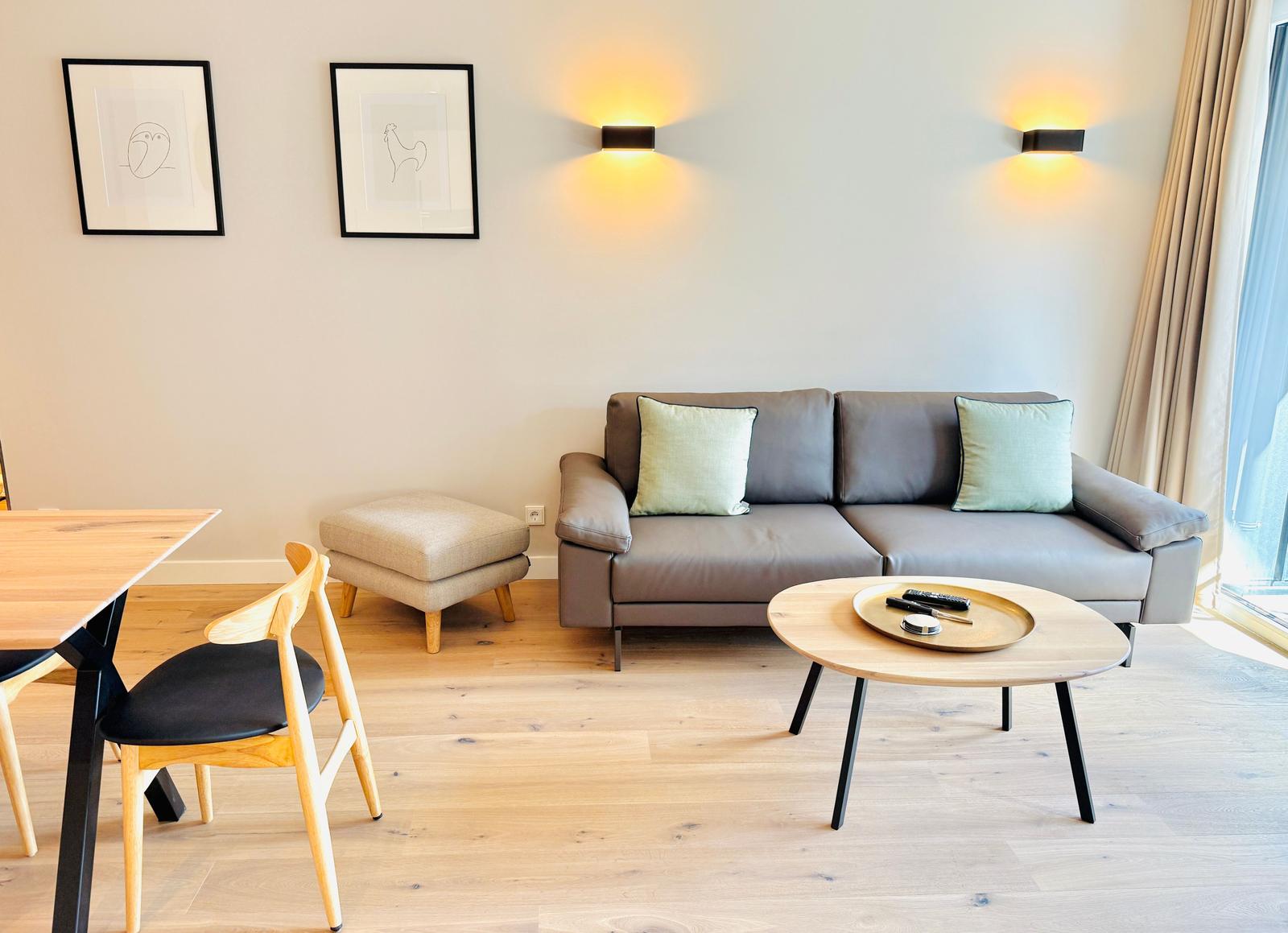 Wohnzimmer mit Sofa, Couchtisch und Stuhl. An der Wand hängen zwei Bilder und zwei Wandlampen.