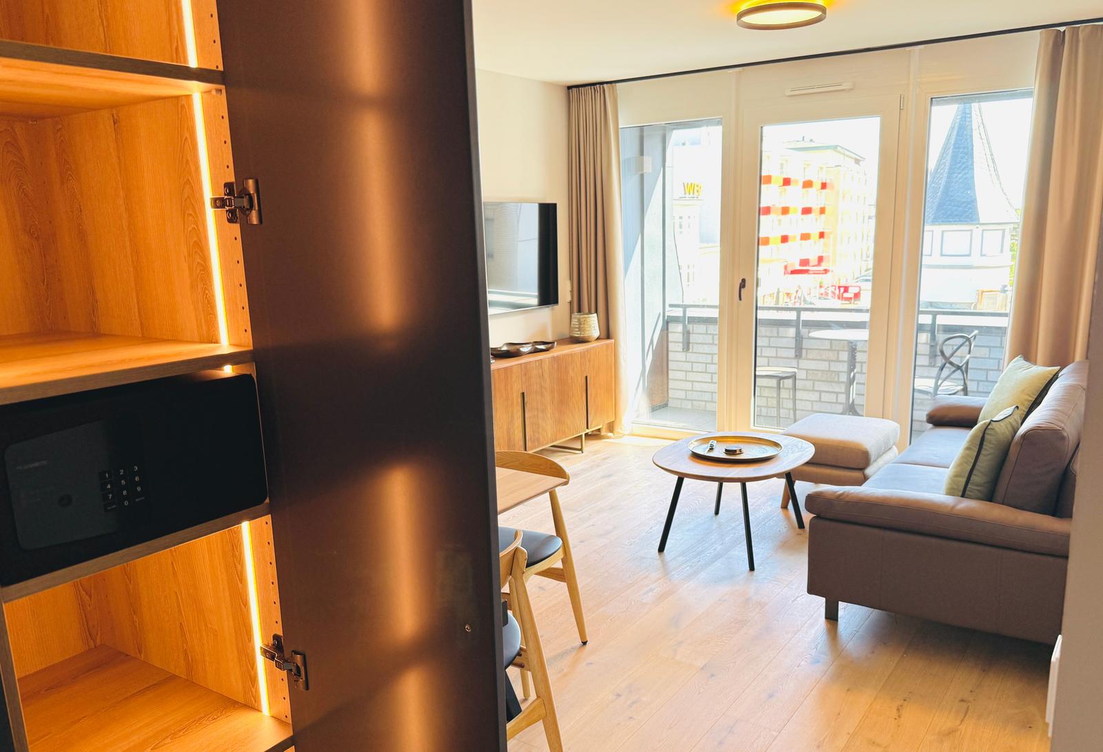 Wohnbereich mit Sofa, Tisch und Balkon. Holzmöbel und integrierte Klimaanlage.