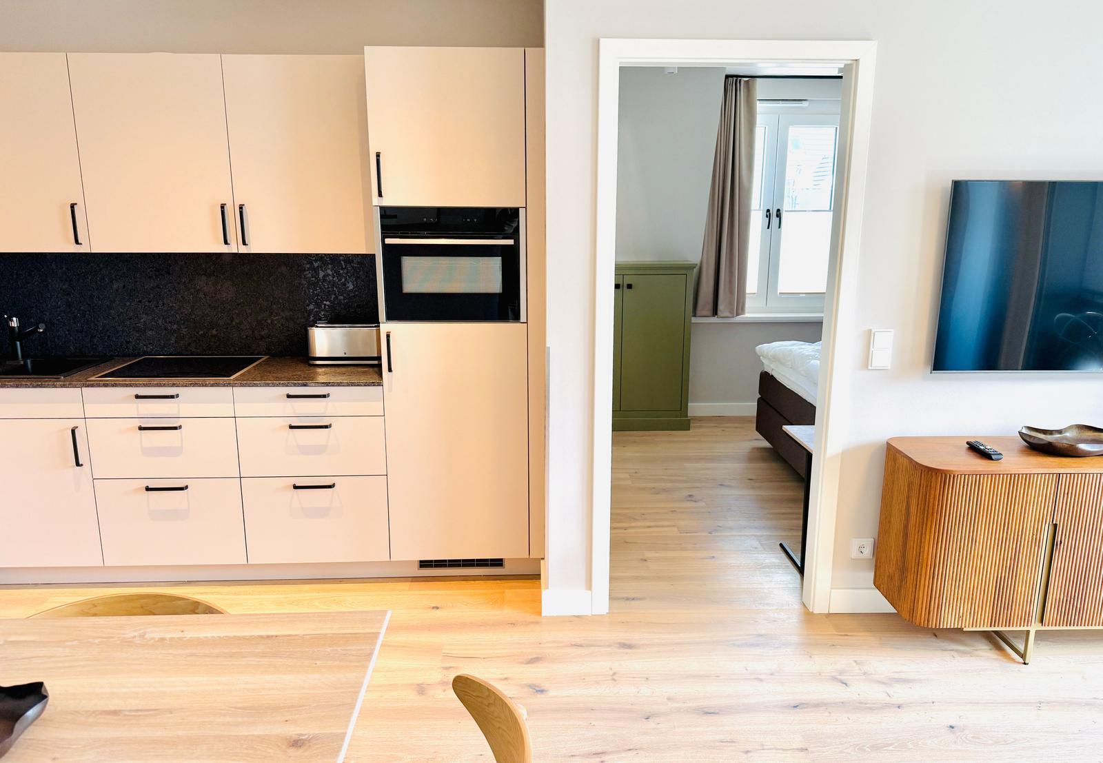 Küche mit Einbauherd, Schlafzimmer mit Bett und Fenster, Wohnbereich mit Fernseher und Holzmöbel.