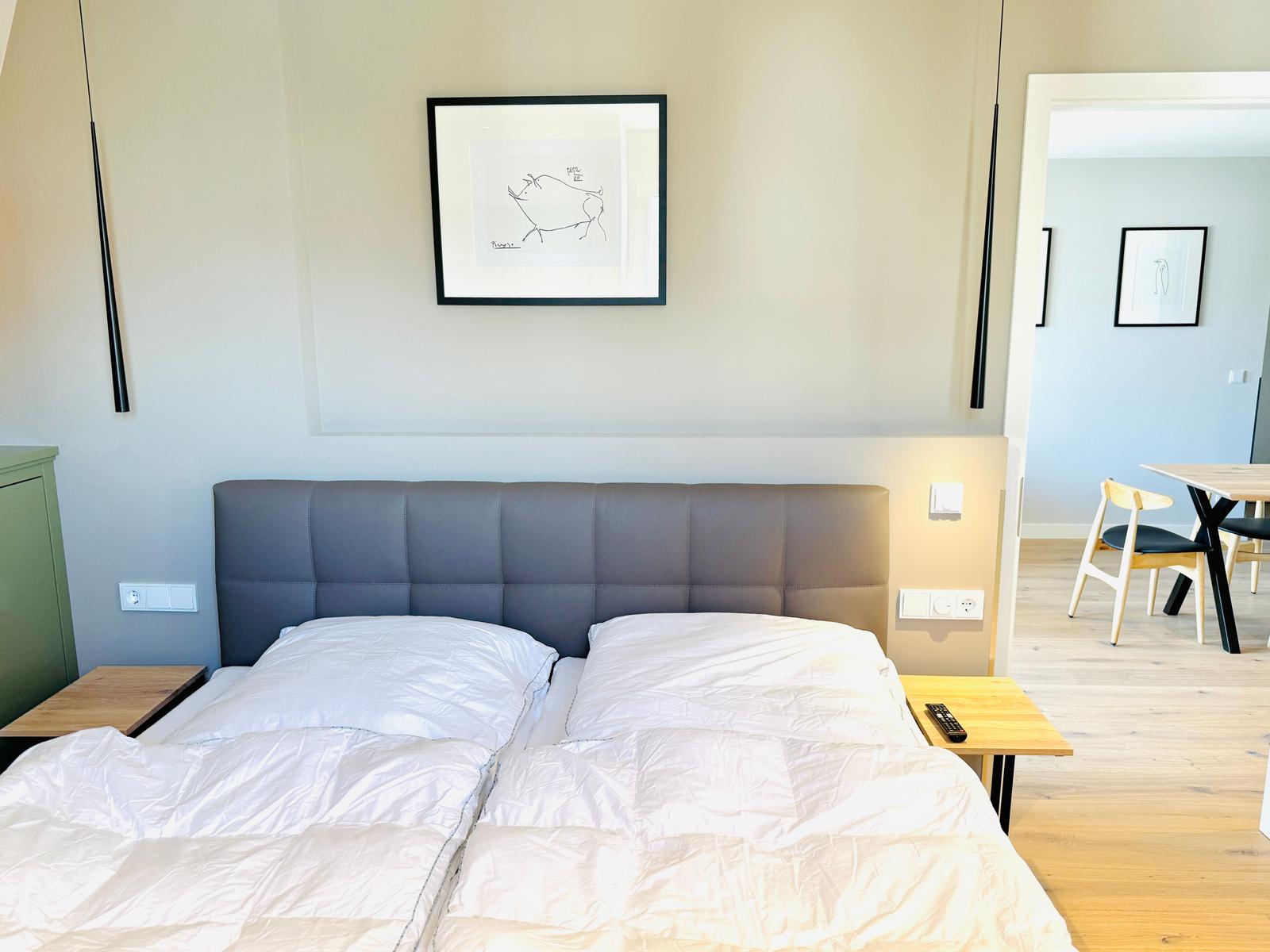 Doppelbett mit weißer Bettwäsche, grauem Kopfteil und Holztischchen.