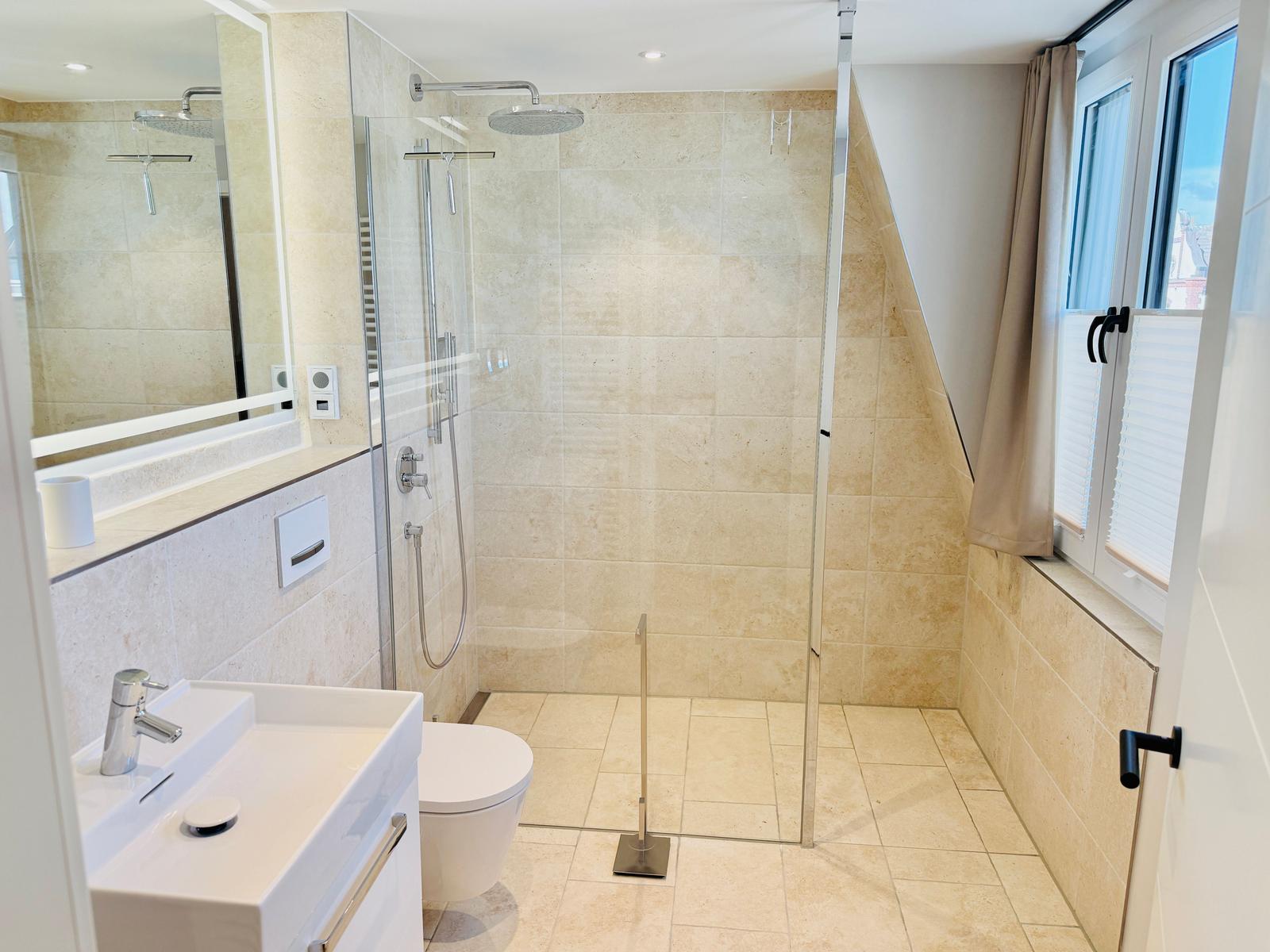 Badezimmer mit Dusche, Waschbecken und Toilette. Fenster mit Vorhängen.