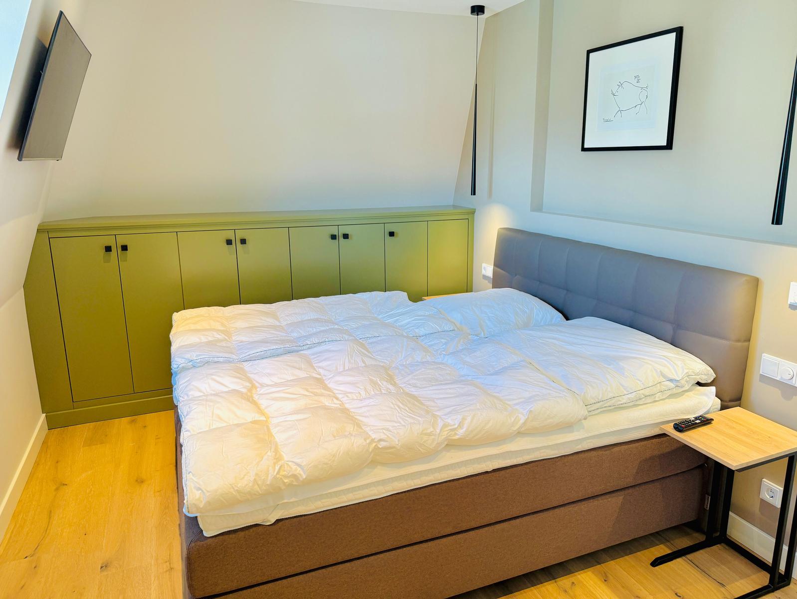 Schlafzimmer mit Bett, grünem Schrank und Wandbild.