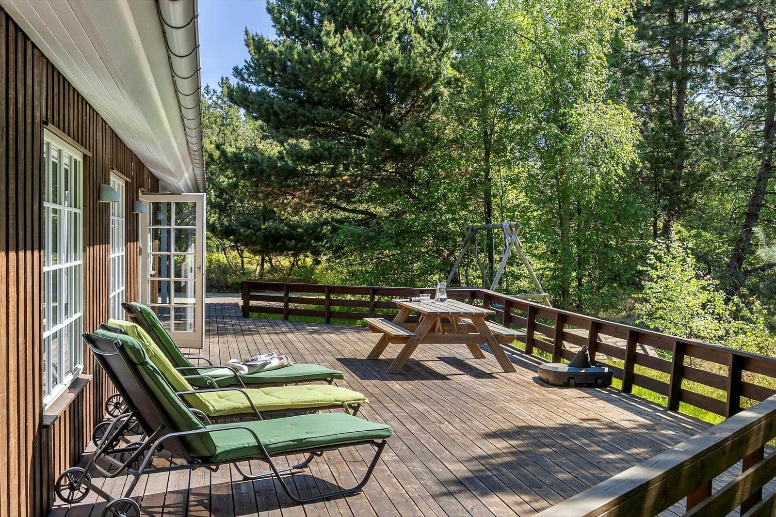 Terrasse mit Liegestühlen, Tisch und Blick in den Wald.