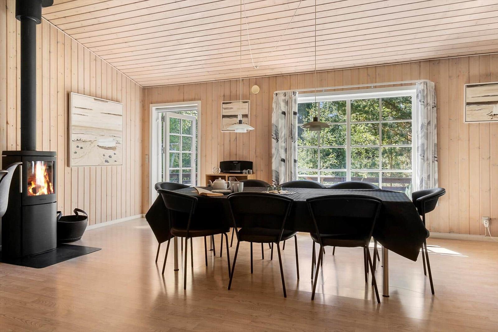 Esszimmer mit Esstisch, Stühlen und Kaminofen. Holzwände und große Fenster.