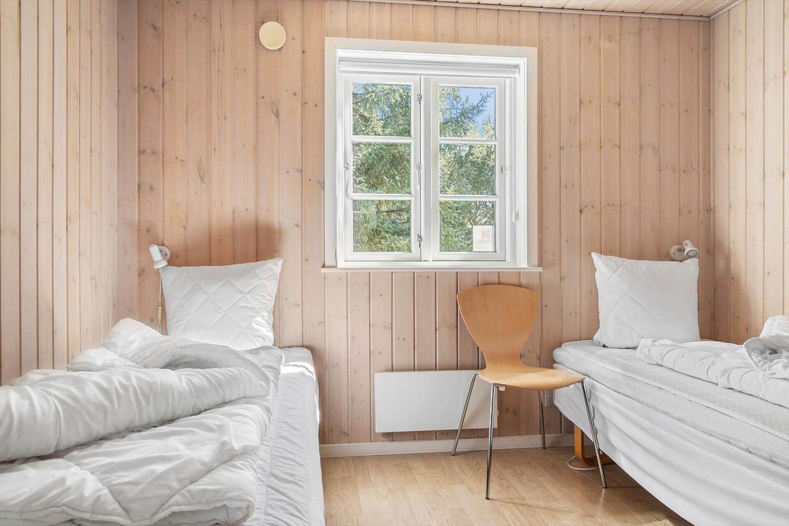 Zwei Betten mit weißen Laken, Holzwand und Fenster mit Blick auf Bäume.