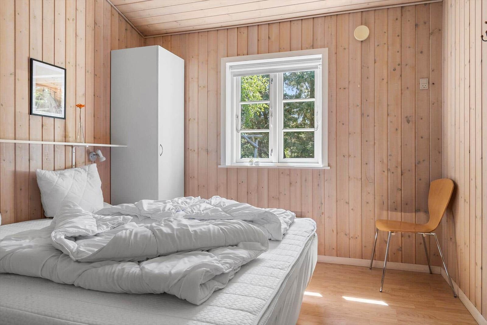 Schlafzimmer mit Holzwand, Bett, Fenster und Stuhl.