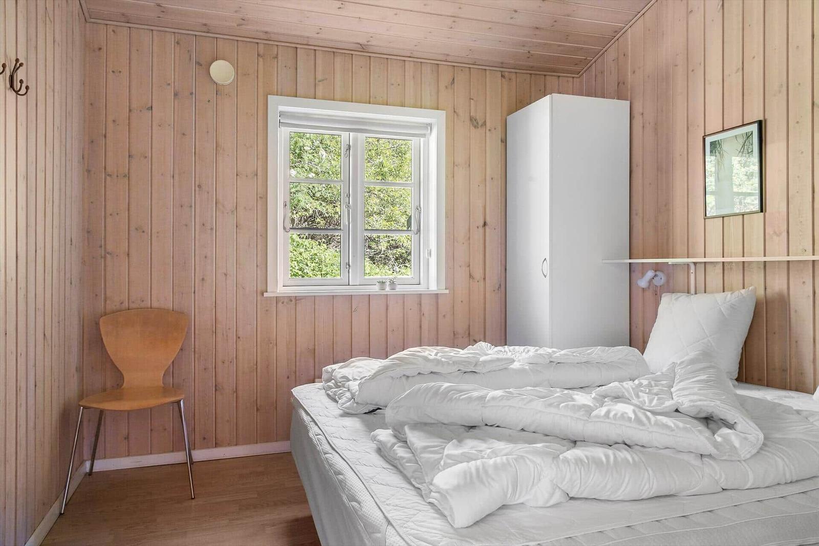 Schlafzimmer mit Holzwand, Bett, Schrank und Fenster mit Blick auf Grün.