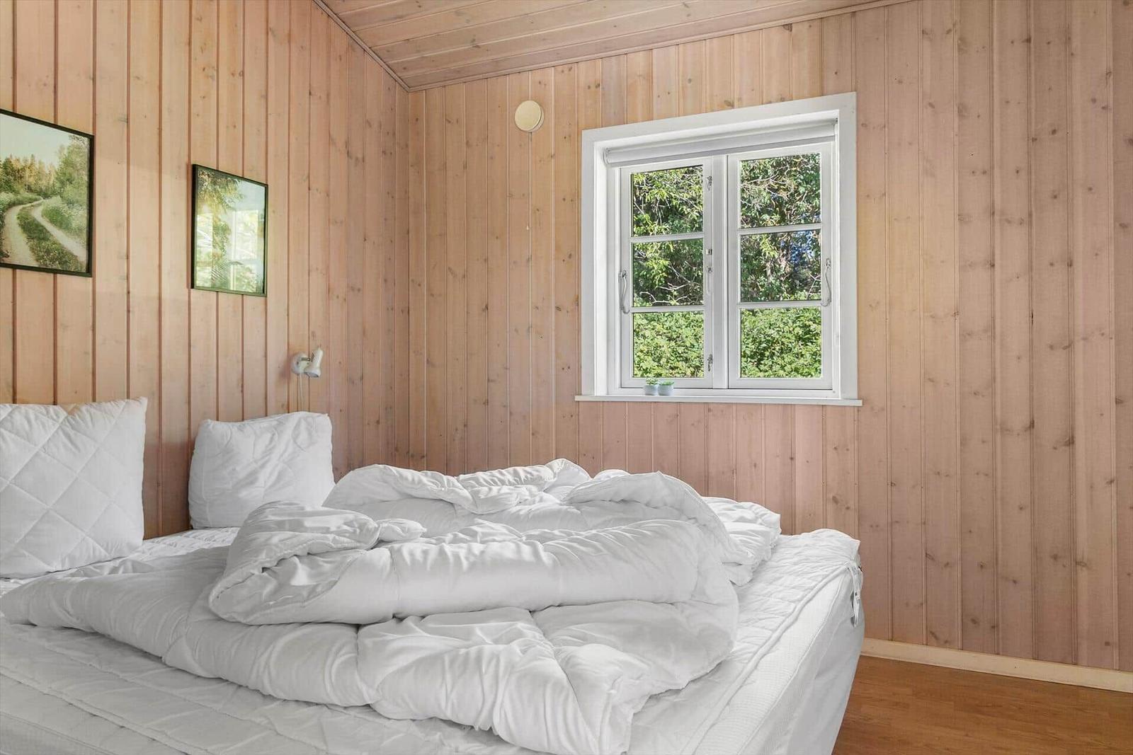Schlafzimmer mit Holzwand, Bett und Fenster mit Blick auf Bäume.