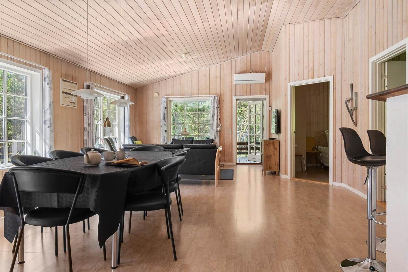 Großes Esszimmer mit Tisch und Stühlen, Wohnbereich mit Sofa und Fenstern, Holzdecke und -wände.
