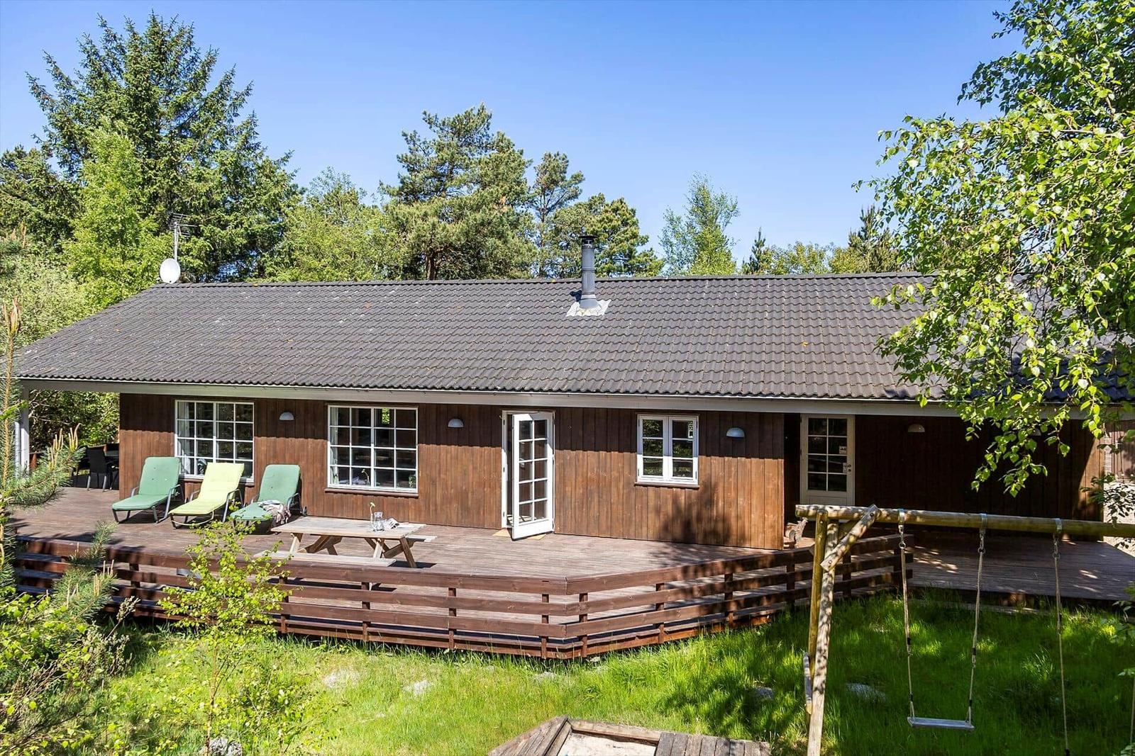 Holzhütte mit Terrasse, Liegen und Schaukel im Grünen.