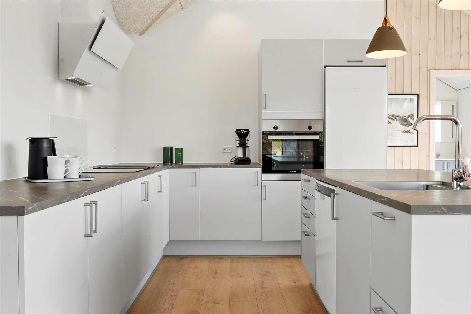 Moderne Küche mit weißen Schränken, Edelstahlgeräten und Holzboden.