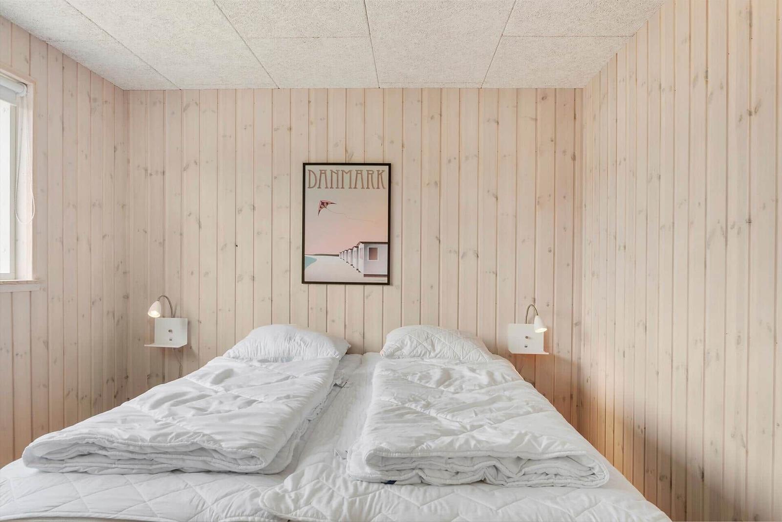 Schlafzimmer mit Holzwand und Bett mit weißen Bettwäsche.