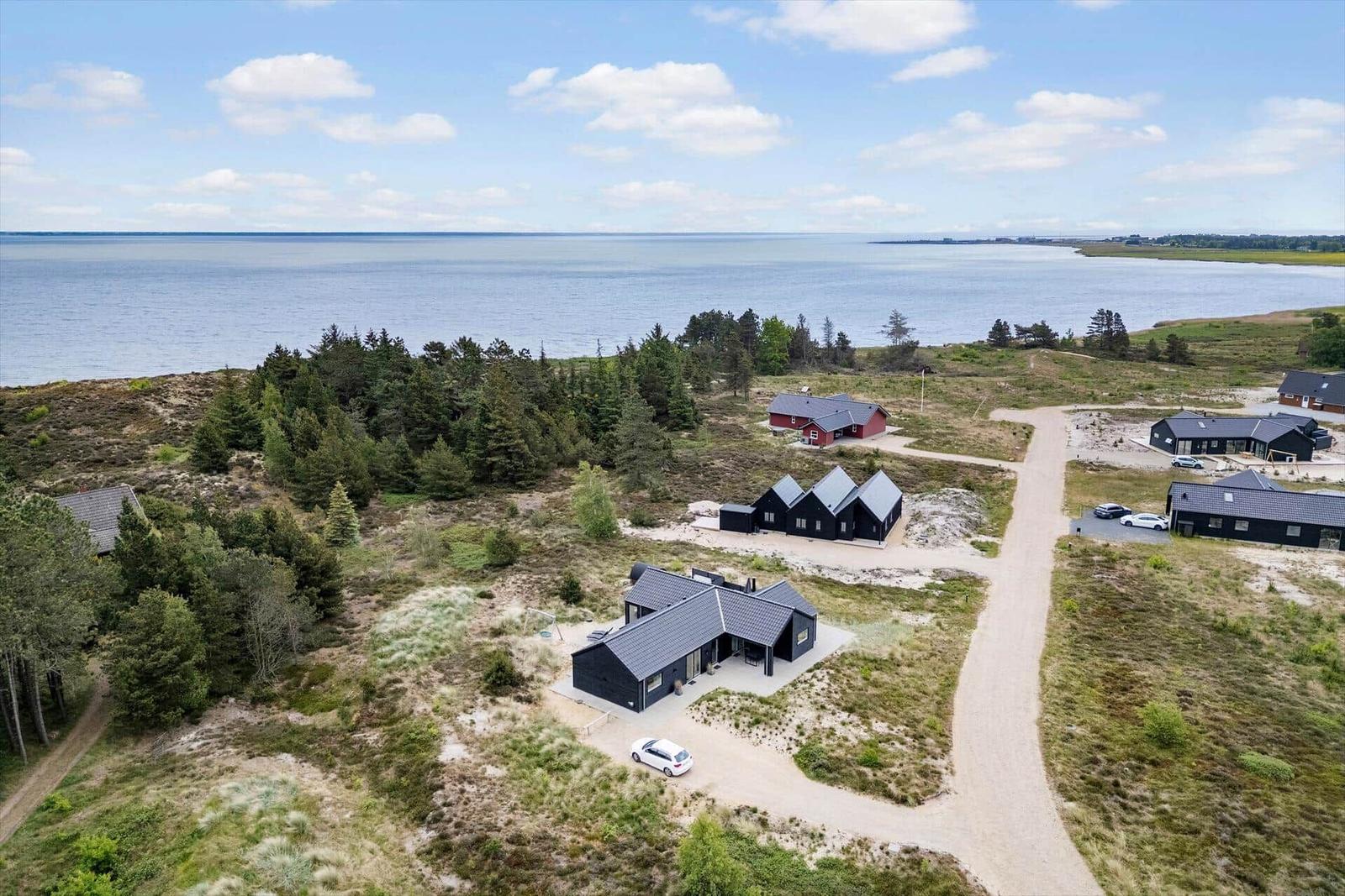 Aerial view of modern cabins near the sea with gravel paths and surrounding greenery.