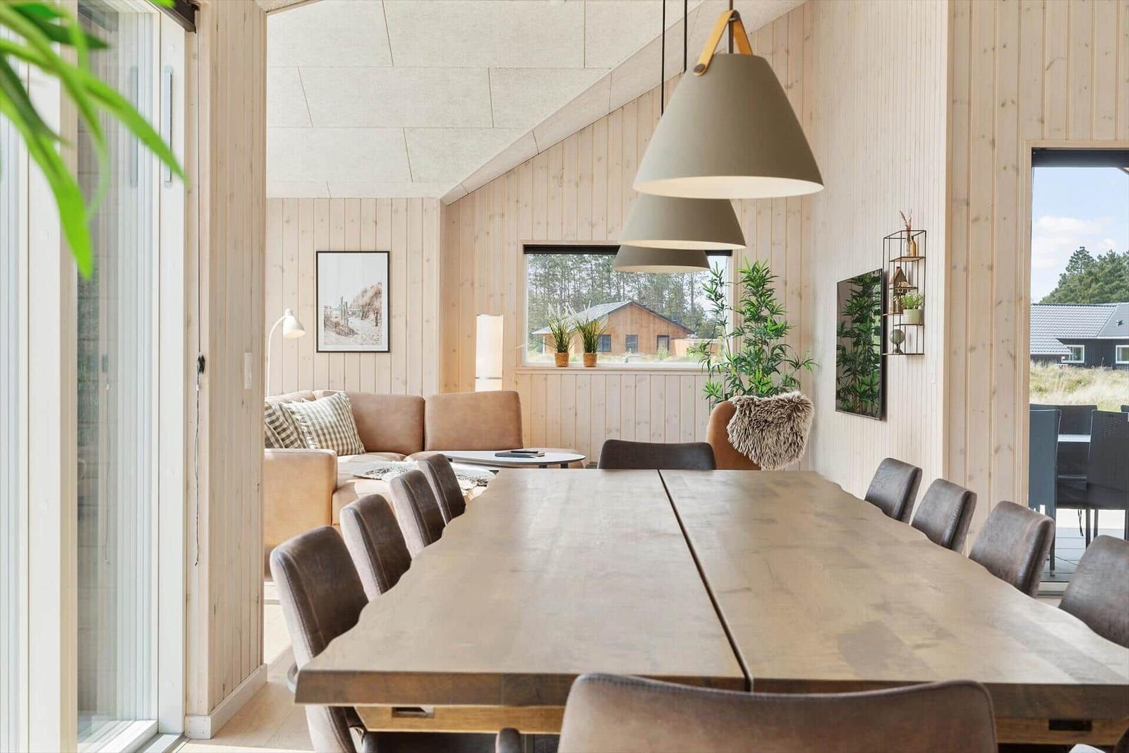 Esszimmer mit großer Holztafel und Sitzgelegenheiten. Holzwände und große Fenster.