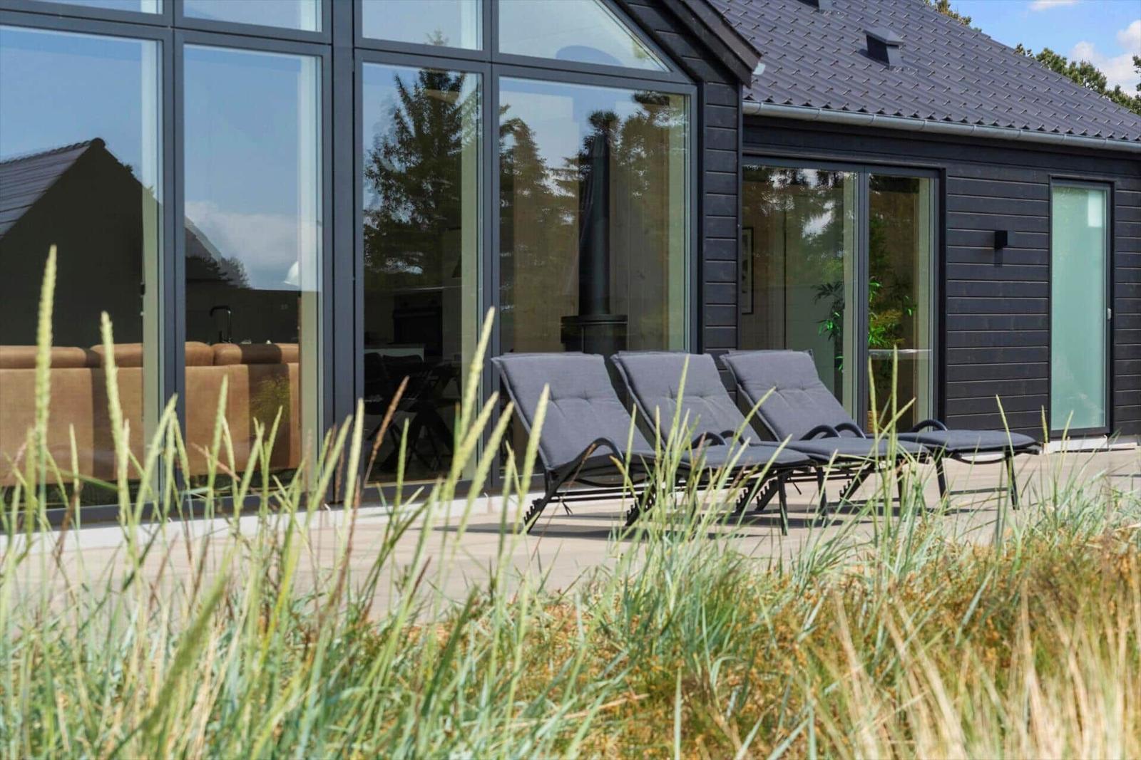 Terrasse mit drei Liegestühlen vor einem modernen Haus mit großen Fenstern.