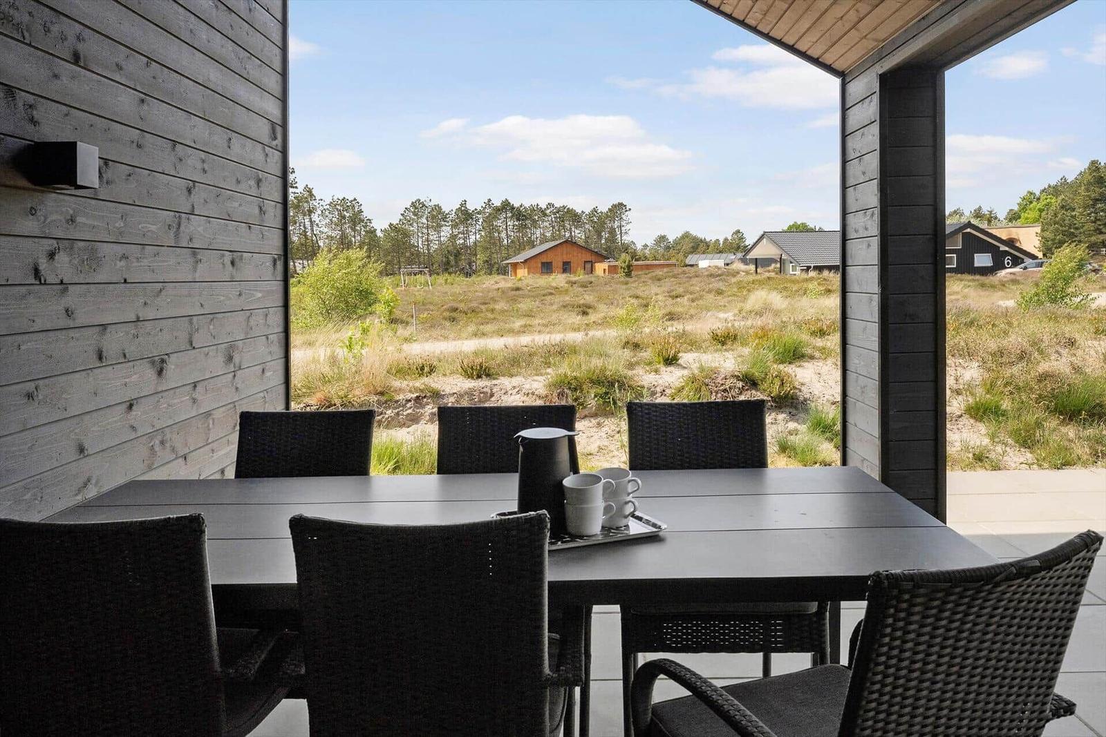 Terrasse mit Tisch und Stühlen, Blick auf Grasland und Bäume.