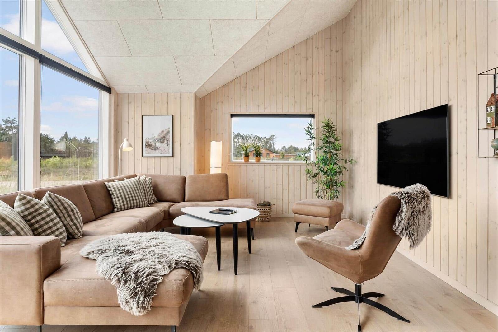 Wohnzimmer mit Sofa, Sessel und Fernseher an Holzwand