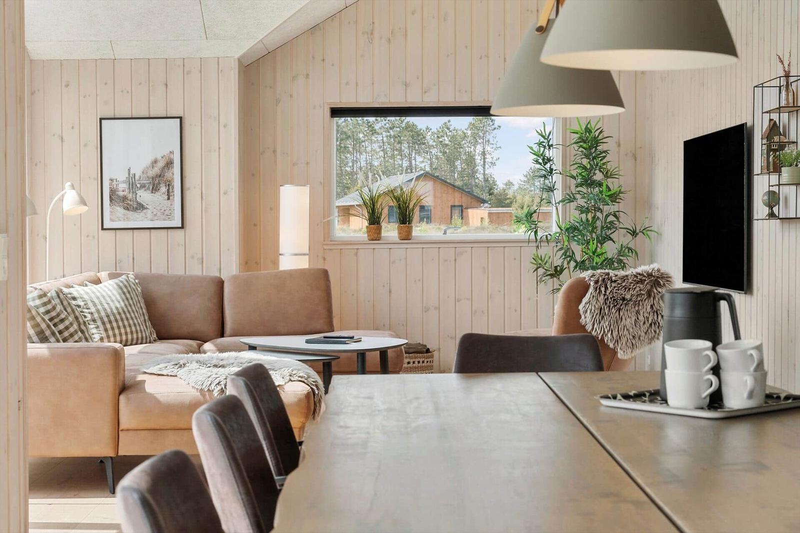 Wohn- und Essbereich mit Holzwand, Sofa, Tisch und Fensterblick.