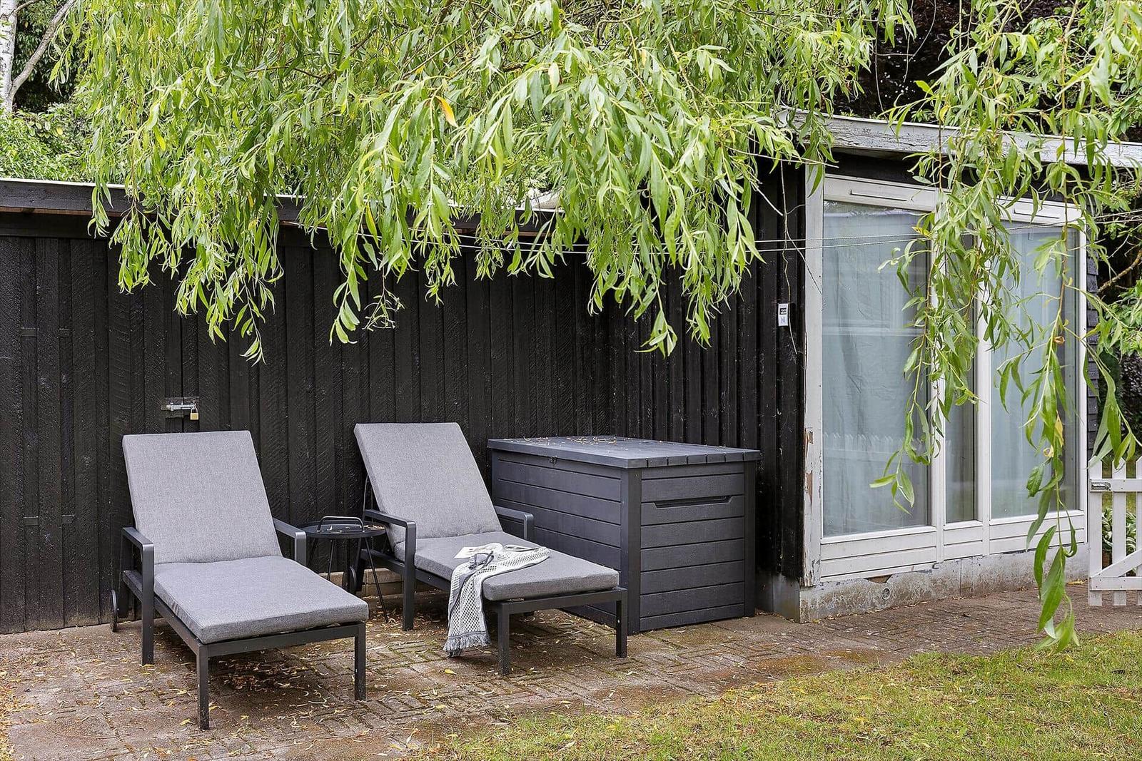 Two lounge chairs under hanging branches in front of a house with sliding door.